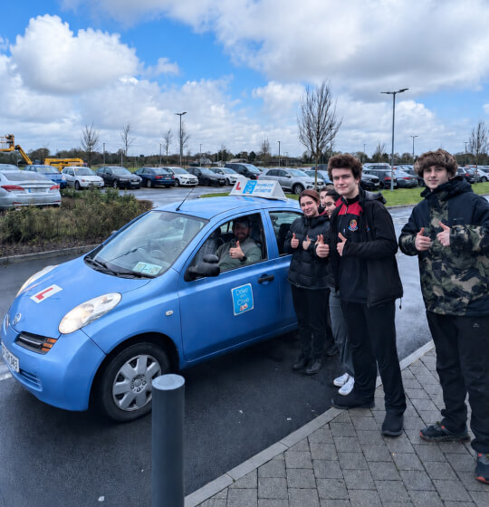 Young learner drivers giving a thumbs up beside the Drive with Clive learner car