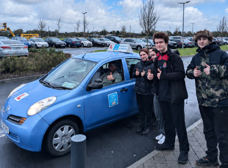 Young learner drivers giving a thumbs up beside the Drive with Clive learner car