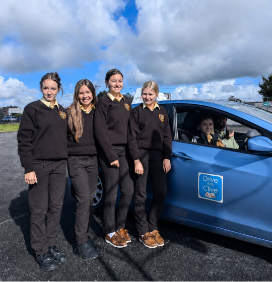 Secondary school students smiling beside the Drive with Clive driving school car